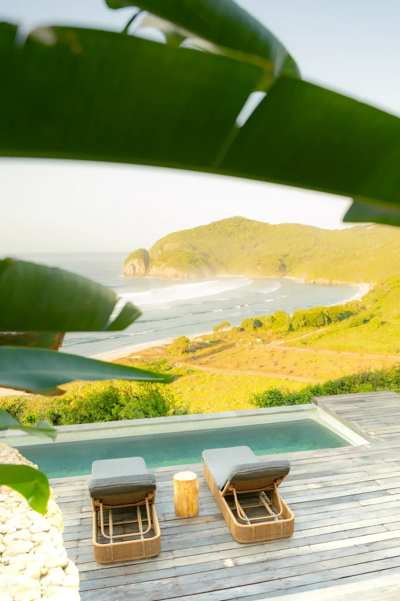 Infinity pool deck overlooking pristine beach through tropical foliage at Elysian Cove