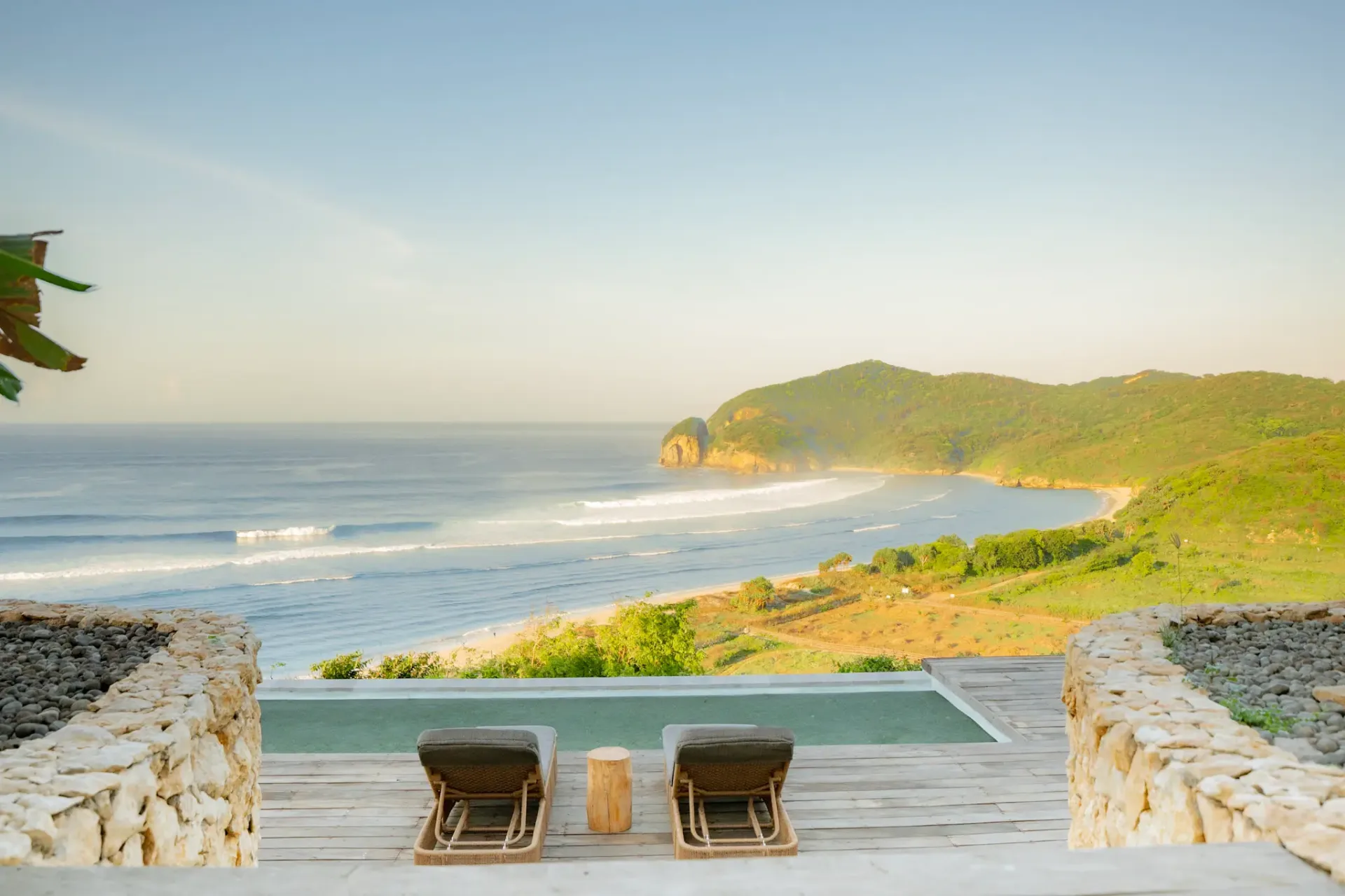 Two lounge chairs face the ocean and green hills at Elysian Cove, a peaceful hotel in Sumbawa offering beachfront accommodation.