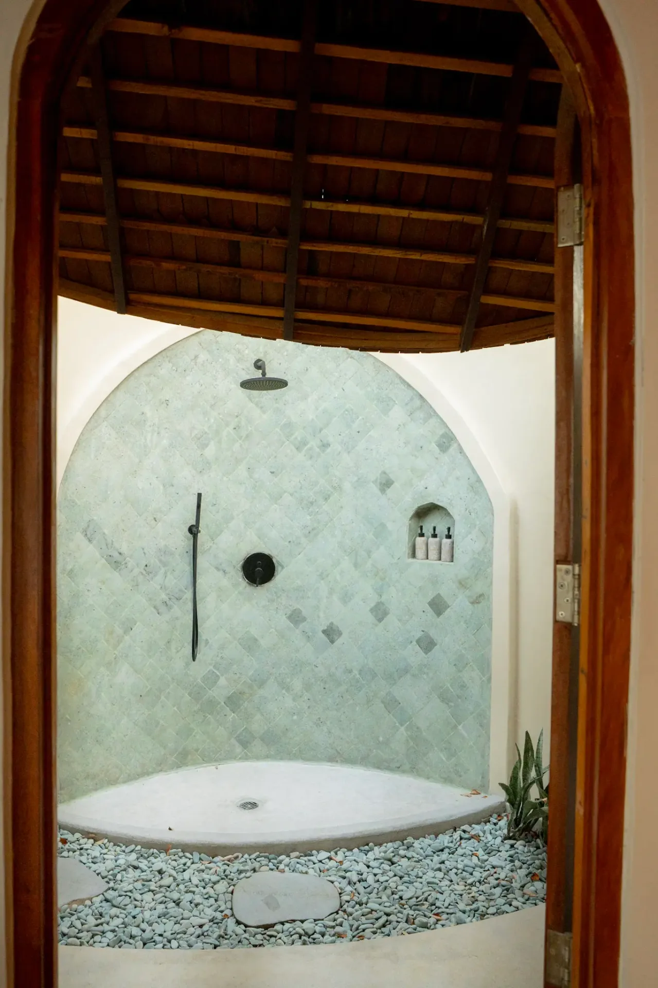 Private outdoor shower with natural stone and wooden ceiling at Elysian Cove villa